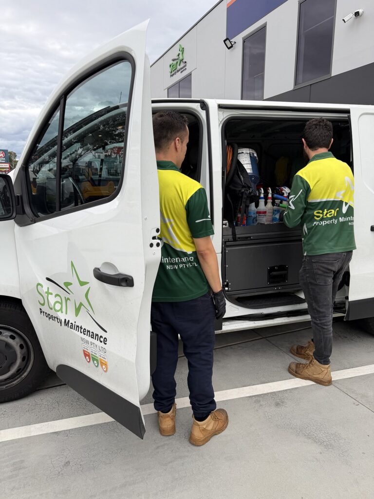 Strata cleaning checklist: Two workers in green and yellow uniforms loading cleaning supplies into a white signwritten work