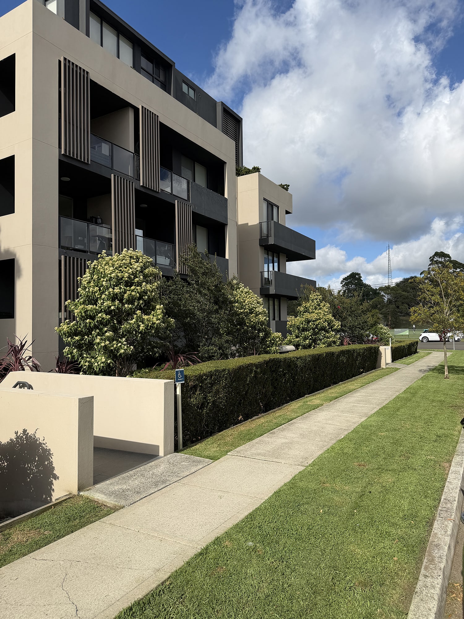Strata cleaning Sydney: a modern apartment block with balconies beside a swept footpath, hedge and lawn